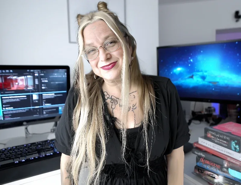 Juliana Loomer smiling at her editing desk, with monitors and a stack of books behind her